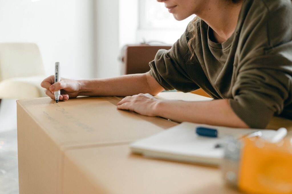 Une personne écrivant sur une grande boîte en carton posé sur une table avec des outils et des documents à côté.